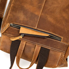 Close-up of the Vintage Leather Backpack crafted from genuine cowhide leather, showcasing dark fabric handles and straps. The image highlights the partially open front zipper pocket, emphasizing the texture and stitching details of this travel essential.