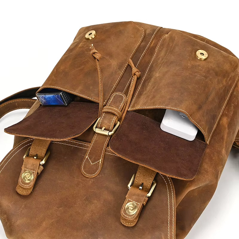 Introducing the Vintage Leather Backpack, crafted from genuine cowhide. It includes two front pockets, with one designed to accommodate a blue rectangular object and the other for a white one. This backpack is ideal for carrying travel essentials and features buckle straps along with metallic button closures.