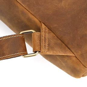 Close-up of a genuine cowhide leather corner from the Vintage Leather Backpack, featuring a metal ring secured by a matching leather strap. The visible stitching showcases the craftsmanship of this travel essential.