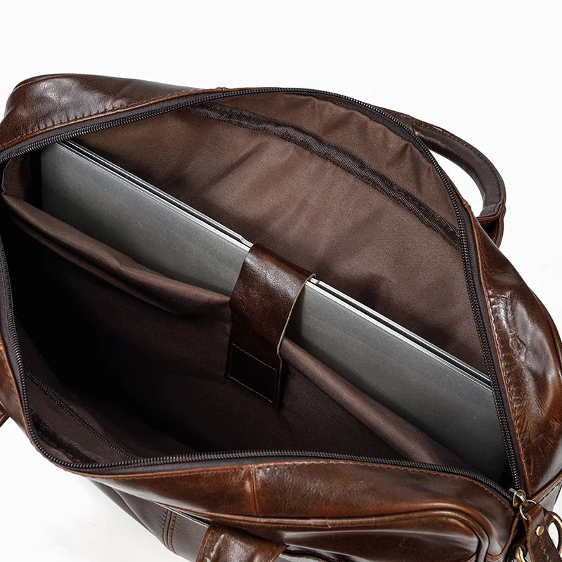 Top view of an open Leather 16" Briefcase made from genuine cow leather, revealing a grey laptop inside a padded compartment. The interior is lined with dark brown fabric and features an adjustable strap to secure the laptop.