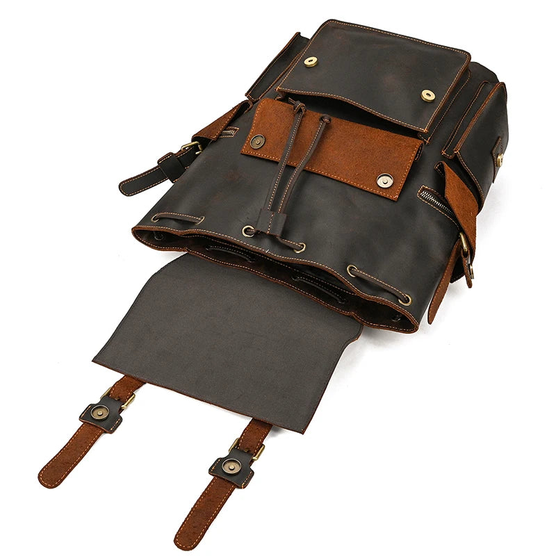 Image of an open Genuine Leather Travel Backpack in dark brown, showcasing its multiple compartments. The main flap is open, revealing an interior drawstring closure and several pockets, including two front pockets with buckle closures and additional side pockets. This vintage backpack ensures both style and functionality.