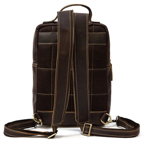 The back view of the Leather Travel Daypack Shoulder Bag showcases a dark brown, rectangular backpack with tan stitching. This versatile daypack features two adjustable, padded shoulder straps, a grab handle at the top, and a mesh back panel for ventilation. The material appears to be made of genuine cowhide leather or high-quality faux leather.