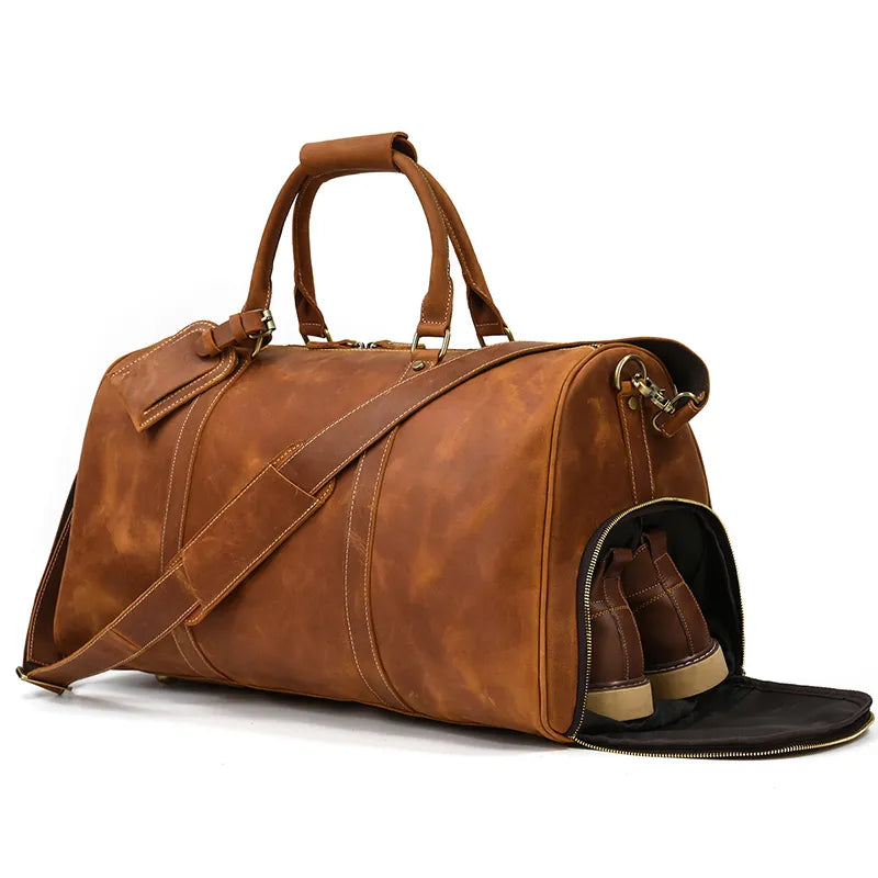 A large brown Weekender 24 Duffle Bag with sturdy handles is pictured. Made from genuine cowhide leather, the bag features a detachable shoulder strap and a zippered compartment at one end, open to reveal a pair of shoes stored inside—perfect for travellers.