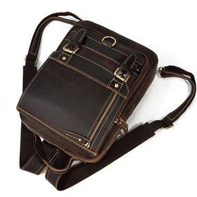 The Leather Travel Daypack Shoulder Bag is crafted from genuine cowhide leather in a dark brown shade, featuring multiple pockets and compartments. It includes gold zippers and buckles, an adjustable shoulder strap, and boasts a sleek, rectangular design. The visible stitching enhances the detailed aesthetics, making it a versatile bag for any occasion.