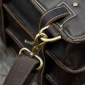 Close-up of the Leather Business Travel Briefcase Backpack, crafted from genuine dark brown cowhide leather. It features a brass clasp and clip attached to a canvas shoulder strap. The white stitching along the edges showcases its high-quality craftsmanship, making it a sturdy and versatile choice for business travel.