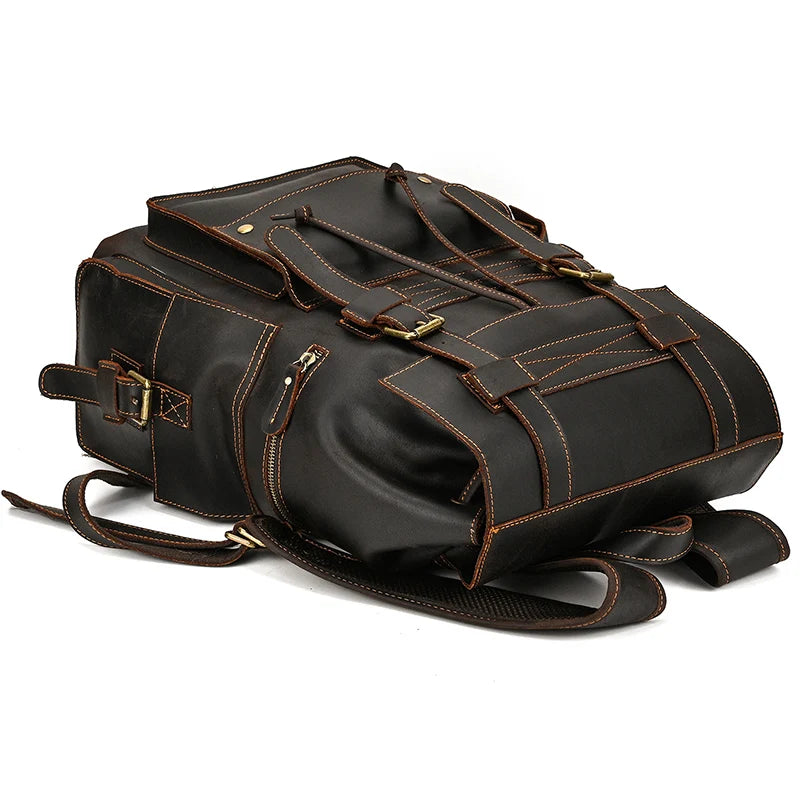 The Genuine Leather Travel Backpack, with its stylish black exterior, is lying on its side. It features elegant brown stitching and buckles, numerous pockets for organization, and easily adjustable straps. The bag boasts a vintage design with metal hardware and a structured shape.