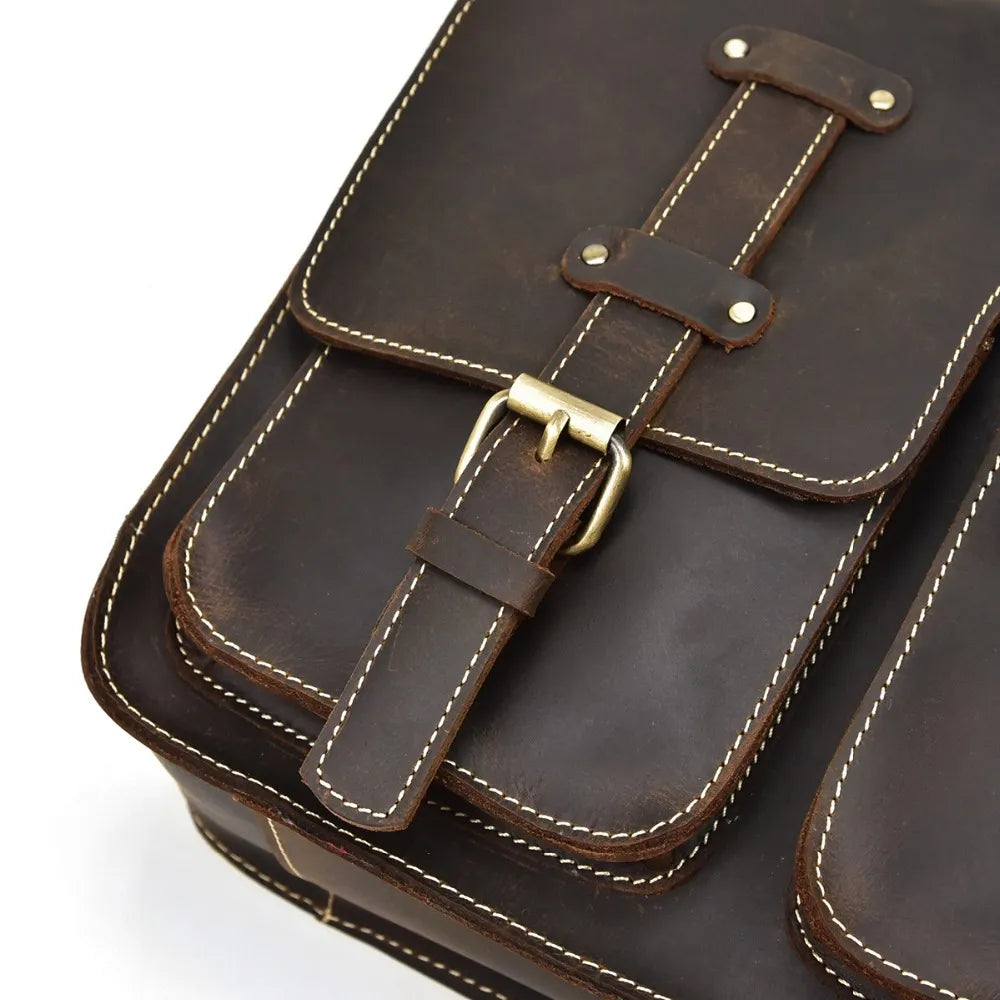 Close-up of the Leather Business Travel Shoulder Bag in dark brown genuine cowhide leather, showcasing its contrasting white stitching. It is equipped with a brass buckle and two front pockets secured with high-quality alloy hardware and metal rivets. The craftsmanship emphasizes the rugged and classic design of this leather shoulder bag.