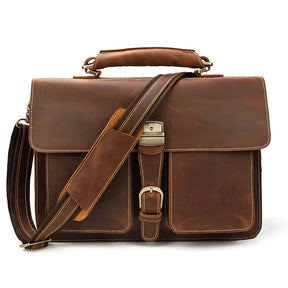 The Leather 16" Business Briefcase is a brown leather satchel equipped with a top handle, adjustable strap, and multiple buckles. It features a front flap secured by a metal clasp and decorative stitching along the edges. Crafted from genuine cowhide leather, the bag has a worn appearance that gives it a vintage look perfect for business use.