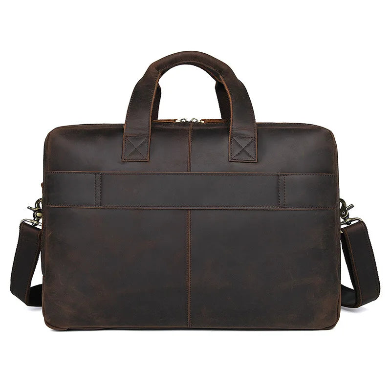 The Leather 17" Business Travel Briefcase is crafted from genuine dark brown leather. It features two top handles and an adjustable shoulder strap for versatile carrying options. The front of the briefcase is adorned with a horizontal strap and visible stitching, while the interior includes a dedicated laptop compartment for easy organization on the go.