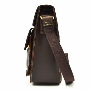 Side view of the Leather Business Travel Shoulder Bag in dark brown, crafted from genuine cowhide leather. It features a wide canvas shoulder strap, detailed stitching, and high-quality alloy hardware including a brass ring securing the strap. The flap is slightly open, highlighting its structured design.