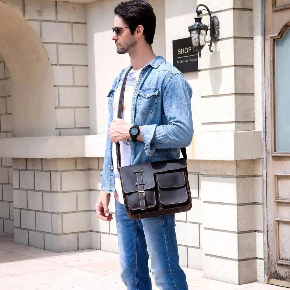 A man wearing sunglasses and a denim jacket stands outside a building, carrying a Vintage Shoulder Bag over his shoulder. A sign with the words "Shop 1" and "American Apparel" is visible in the background. The man glances to his right, as if contemplating business trips ahead.