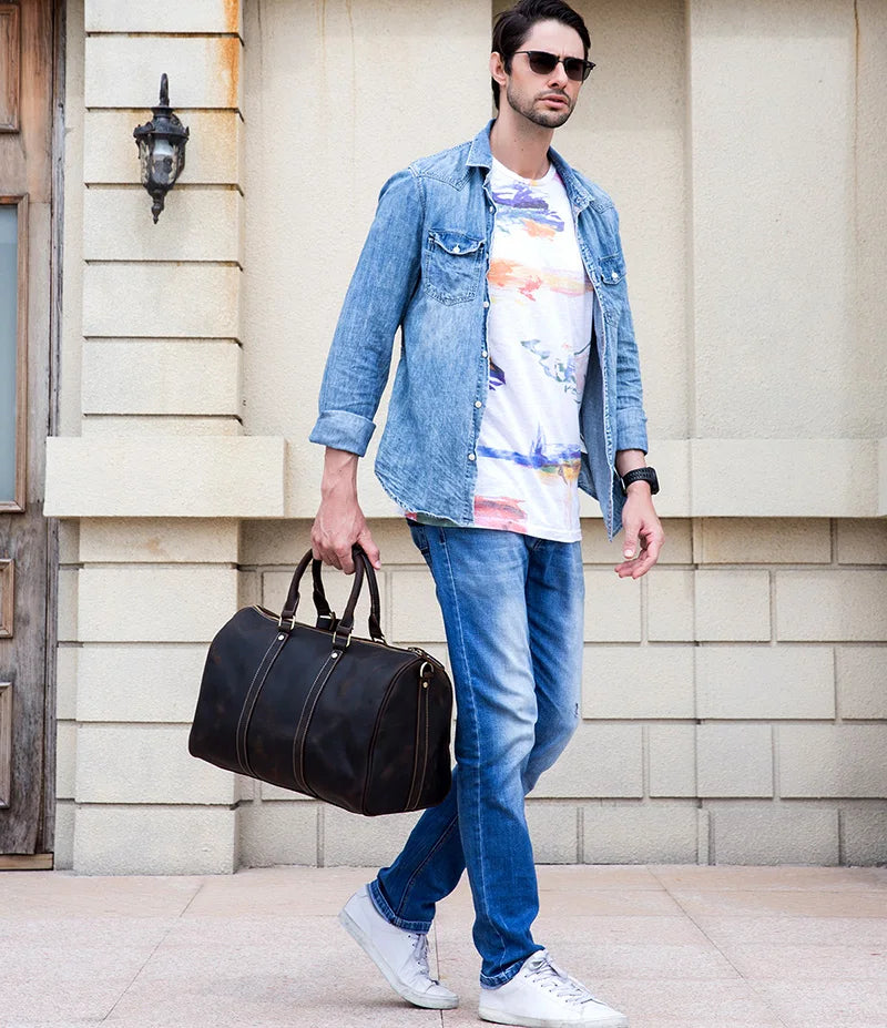 Man carrying Weekender 18 Leather Bag made from 100% genuine cowhide leather, wearing casual outfit and sunglasses.