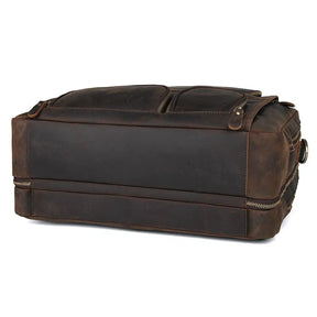 The Leather 17" Business Travel Briefcase is a sturdy, dark brown leather duffel bag with a rugged appearance, shown from a side angle. It features a reinforced base, a laptop compartment, two zippered pockets on one side, and leather handles. The worn look adds to its vintage charm.