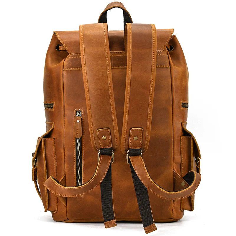 The Genuine Leather Travel Backpack is crafted from durable cow leather and includes adjustable shoulder straps, a convenient top handle, side pockets with buckle accents, and a front zippered compartment. Its back view boasts vintage aesthetics with strong stitching and black fabric lining the underside of the straps.