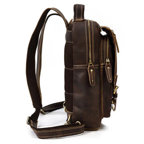 Side view of the Leather Travel Daypack Shoulder Bag, crafted from genuine brown cowhide leather. This versatile backpack showcases two zippered compartments, adjustable shoulder straps, and detailed stitching. It features zippers with leather pulls, a padded mesh panel for comfort, and brass buckles and accents.