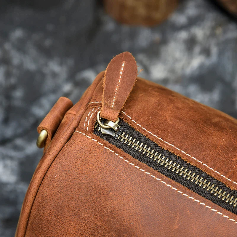 Close-up image of the Weekender 18 Leather Bag in genuine cowhide leather featuring a zipper with a leather pull tab. The stitching is visible, showcasing a rustic and rugged design. The background is blurred, keeping the focus on the detail of the bag and its spacious interior pockets.