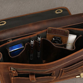 A close-up view of the interior of an open Vintage Leather Briefcase, showcasing organized compartments. It contains pens, a deck of cards, a tube of cream, and a pocket with a small black item. The neatly arranged interior exudes a professional image and includes a laptop compartment for added functionality.