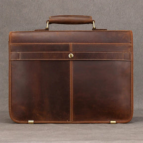 The Vintage Leather Briefcase is photographed against a plain gray background, showcasing its genuine leather material and single top handle. The briefcase features a minimalist design with clean lines, a snap closure, visible stitching, and a laptop compartment to maintain a professional image.