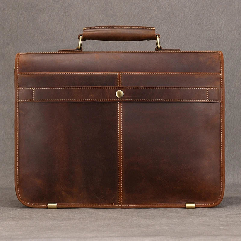 The Vintage Leather Briefcase is photographed against a plain gray background, showcasing its genuine leather material and single top handle. The briefcase features a minimalist design with clean lines, a snap closure, visible stitching, and a laptop compartment to maintain a professional image.