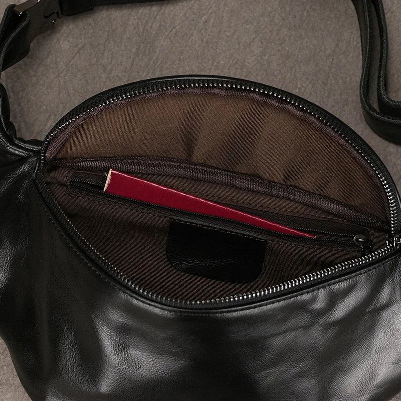 The Leather Belt Bag, made of genuine cowhide leather with a black adjustable strap and durable alloy hardware, lies open, revealing its brown inner lining. Inside the main compartment, a red passport is visible, partially tucked into an inner zipper pocket.