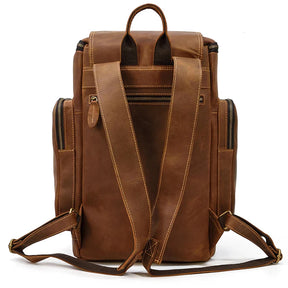 The Vintage Leather Travel Backpack is made from genuine cowhide leather and has padded shoulder straps, multiple zippered pockets, a laptop compartment, a top carry handle, and contrasting stitching. It's photographed from the back to showcase its timeless design.