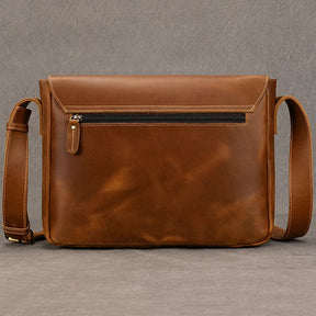 The Vintage Leather Shoulder Bag boasts a sleek design with an adjustable strap and a horizontal zipper pocket on the front. Made from genuine cow leather, this brown satchel features a smooth, polished finish with subtle stitching accents against a neutral grey background for timeless appeal.