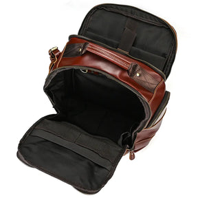 The Vintage Leather Travel Backpack is shown open, revealing a spacious and organized black fabric interior. The main compartment and front pocket are both unzipped, displaying inner pockets and mesh storage areas, emphasizing the ample storage available.