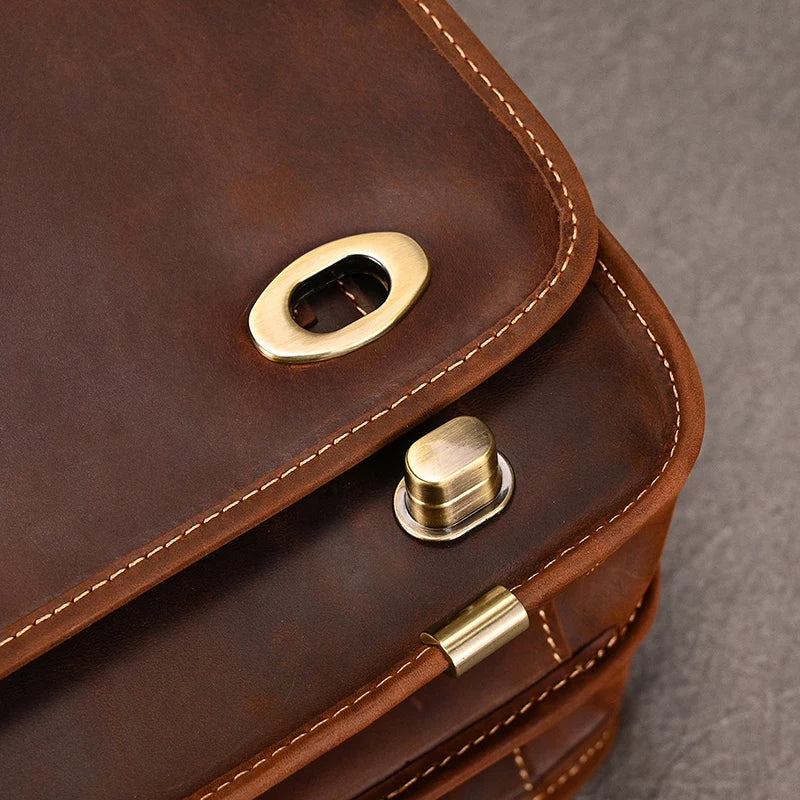 Close-up of a Vintage Leather Briefcase, focusing on its brass hardware. The professional image showcases a rounded brass buckle and a push-lock mechanism for securing the flap. The stitching along the edges and the smooth texture of the leather are clearly visible.