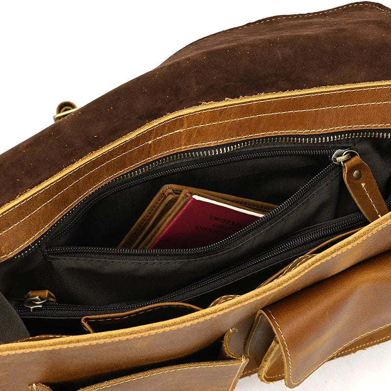 The Leather Business Travel Shoulder Bag, crafted from genuine cowhide leather, is displayed open, showcasing several compartments lined with black fabric. A British passport can be partially seen through an unzipped pocket. The bag has a rugged appearance with visible stitching and a weathered texture.