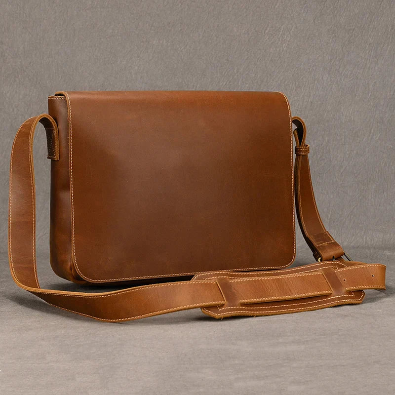 The Vintage Leather Shoulder Bag features a long adjustable strap and is meticulously crafted from genuine cow leather. It showcases a clean, smooth front flap, set against a plain gray background, exuding timeless style.