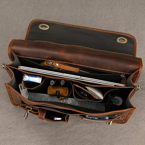 A top-down view of the Vintage Leather Briefcase reveals its spacious and neatly organized interior, boasting a dedicated laptop compartment, wallet, sunglasses, a book, smartphone, loose papers, and various small items meticulously arranged in pockets. It projects a professional image throughout.