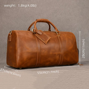 The Weekender Duffle 22 Leather Travel Bag is prominently displayed against a gray background. This large brown bag, made from genuine cowhide leather, includes a handle on top, a detachable shoulder strap, and a luggage tag. Its dimensions are 55cm (21.7 inches) in length, 28cm (11 inches) in height, and 27 cm (10.6 inches) in width.