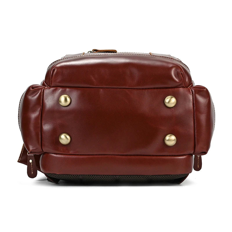 The Vintage Leather Travel Backpack, crafted from genuine cowhide leather and showcased from its bottom side, features brass-colored button feet. This stylish brown backpack boasts a sleek and polished finish, well-defined contours, ample storage space, and additional side pockets for added convenience.