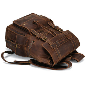 A rugged, light brown genuine leather travel backpack with multiple pockets and buckles laid flat on its back. The durable Genuine Leather Travel Backpack's straps and many storage compartments suggest its suitability for heavy-duty use or outdoor adventures.