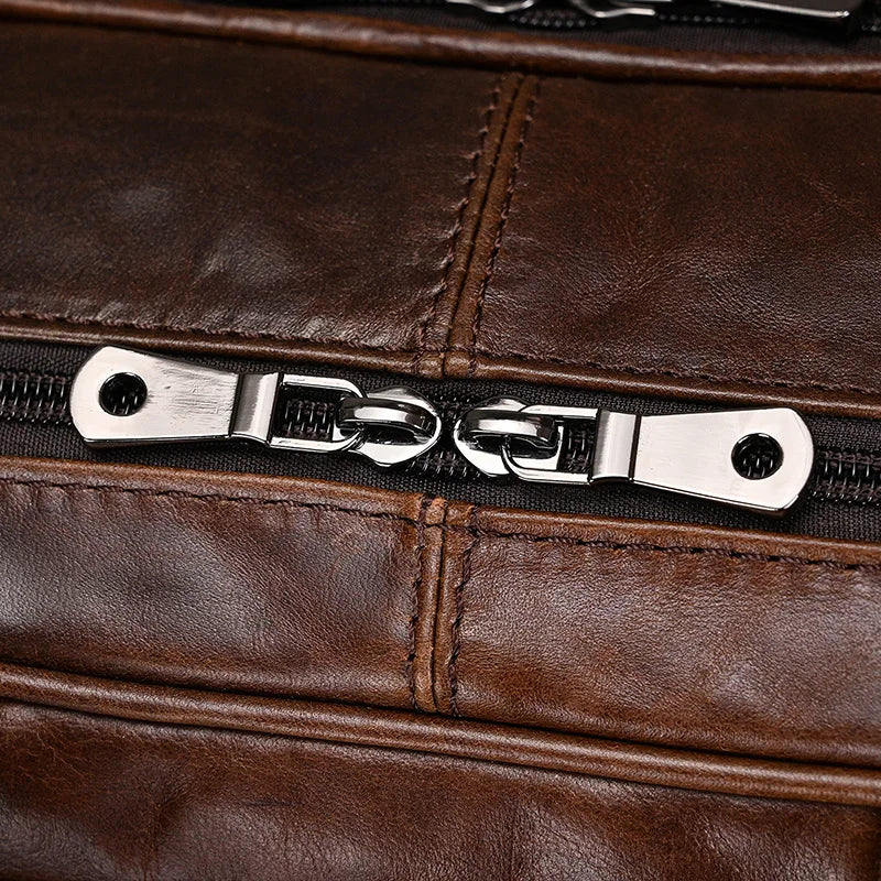 Close-up of the Leather 17" Business Travel Briefcase in dark brown genuine leather with silver metal zippers. The briefcase features a double-zipper mechanism where two zipper pulls meet in the middle. The genuine leather has visible stitching and a slightly worn appearance, indicating use or vintage style.