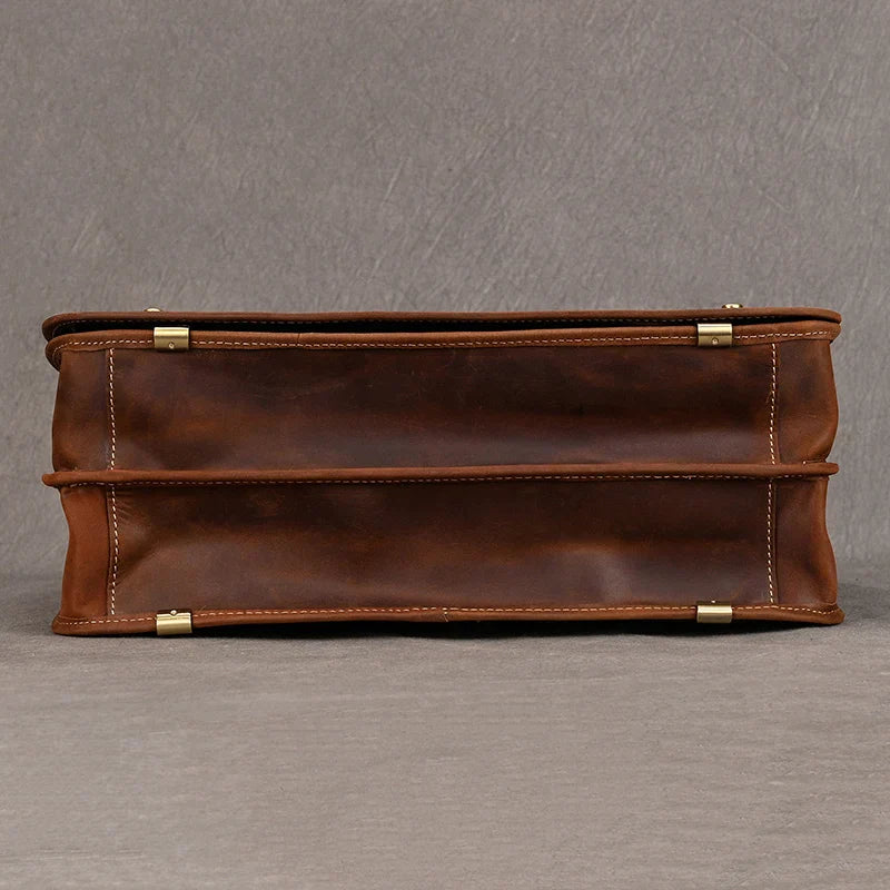 A rectangular, brown Vintage Leather Briefcase is displayed lying flat against a gray background. This genuine leather briefcase boasts a smooth texture, metal corner accents, and visible stitching along the edges. Ideal for maintaining a professional image, the bag also features a dedicated laptop compartment.