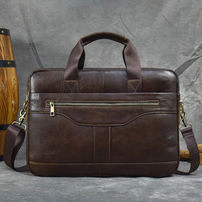 The 16" Brown Leather Briefcase is a stylish genuine leather handbag featuring a zippered front pocket and dark brown handles. It includes an adjustable, detachable shoulder strap with brass hardware and is showcased against a simple gray background.