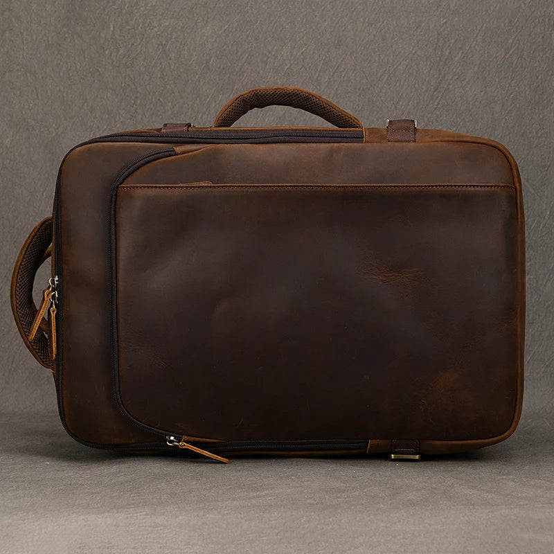 A Vintage Leather Travel Backpack in brown, featuring a handle and two zippers, set against a plain background. The leather showcases a smooth, polished finish, giving the backpack a timeless appeal and medium size.