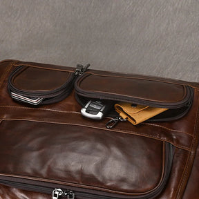 A close-up image of the Leather 17" Business Travel Briefcase in brown genuine leather, showcasing two partially open zippered pockets. The pockets reveal items such as a metallic key, a yellow cloth, and a book against a soft textured gray background.