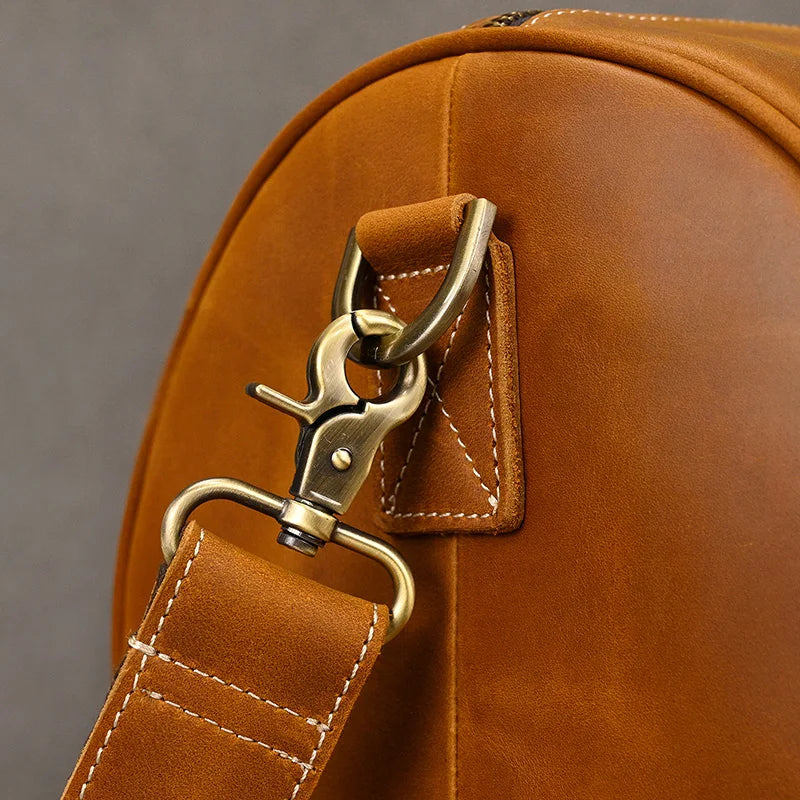 Close-up of a vintage Leather Travel Duffle in brown leather, featuring a metal clasp and strap. Visible stitching highlights expert craftsmanship. The focus on the attachment point emphasizes the bag's quality and design—ideal for stylish travel enthusiasts.