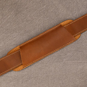 A handle wrap for the Weekender Duffle 22 Leather Travel Bag, crafted from genuine brown cowhide leather, is shown laying on a gray surface. The rectangular wrap with rounded edges and beige stitching along its borders is designed to provide a comfortable grip and protect the bag handle.