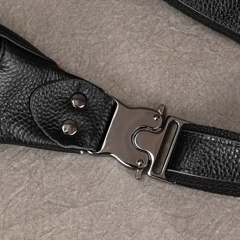 Close-up of a black premium leather strap with a silver metal buckle and snap fasteners. The strap, part of the versatile Black Leather Belt Bag, is lying on a textured gray surface. The silver buckle has a unique, sturdy design.