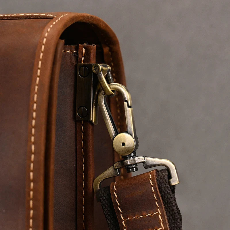 Close-up of the Vintage Leather Briefcase in brown genuine leather, highlighting a metal clasp and intricate stitching detail. The clasp, which connects a fabric strap to the bag, features brass components and is secured with rivets, revealing high craftsmanship and sturdy construction. An ideal accessory for maintaining a professional image.