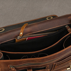 A top view of an open Vintage Leather Briefcase reveals multiple compartments and pockets, some with zippers. Inside, a glimpse of items including a red object can be seen, alongside a dedicated laptop compartment. The briefcase is placed on a grey surface, exuding a professional image.