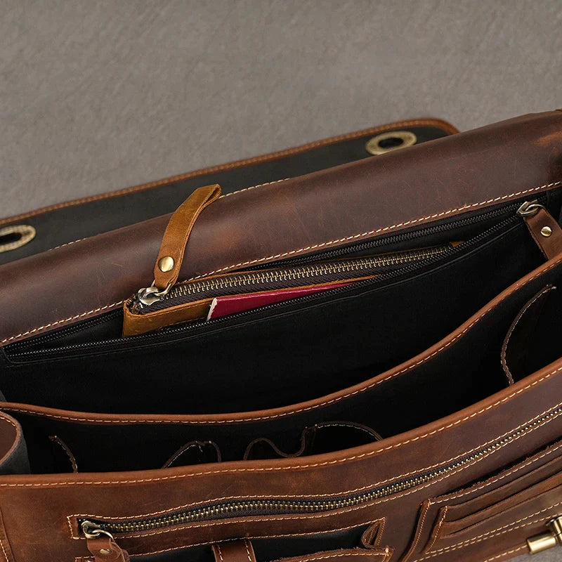 A top view of an open Vintage Leather Briefcase reveals multiple compartments and pockets, some with zippers. Inside, a glimpse of items including a red object can be seen, alongside a dedicated laptop compartment. The briefcase is placed on a grey surface, exuding a professional image.