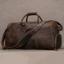 The Weekender Duffle 22 Leather Travel Bag, a large travel bag crafted from dark brown genuine cowhide leather, is displayed against a plain background. It features a sturdy handle, a detachable shoulder strap with a padded section, and a side zipper pocket. Additionally, the bag includes an attached leather luggage tag.