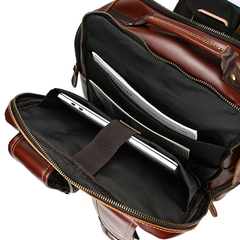 A top-down view of the Vintage Leather Travel Backpack, made from genuine cowhide leather, reveals its ample storage. Inside, a laptop is secured in a padded compartment, along with a few documents in an adjacent pocket. The interior has a black lining and the bag features gold-colored zippers.