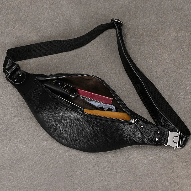 A Black Leather Belt Bag, made from premium leather, is open to reveal its contents: a pair of glasses, a red item, and a black electronic device, possibly a phone. The versatile design includes an adjustable strap with a silver buckle, all laid out on a textured gray surface.