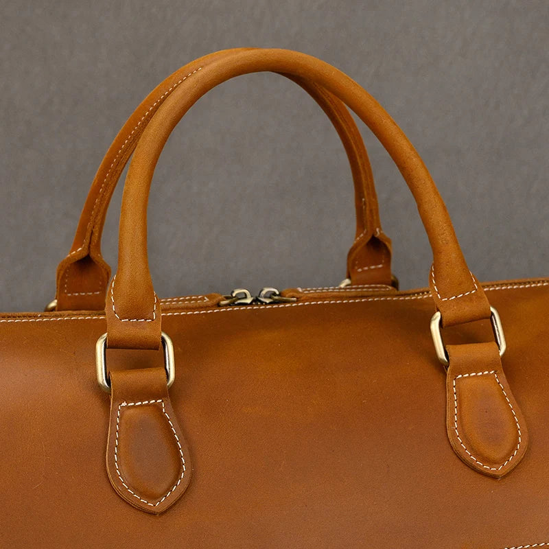 Close-up of a vintage brown Leather Travel Duffle with two sturdy handles and silver buckles against a neutral backdrop. This travel-friendly bag features detailed edge stitching, highlighting its genuine leather craftsmanship.