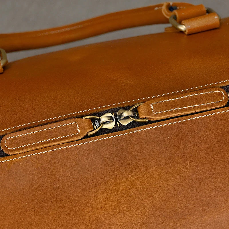 Close-up of the Leather Travel Duffle, highlighting its brown genuine leather with a smooth vintage feel, featuring a metallic zipper and contrasting white stitching. The centered image captures the zipper pull.